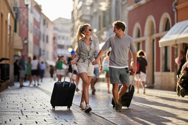 Happy couple of tourists talking while dragging their suitcases on the street.